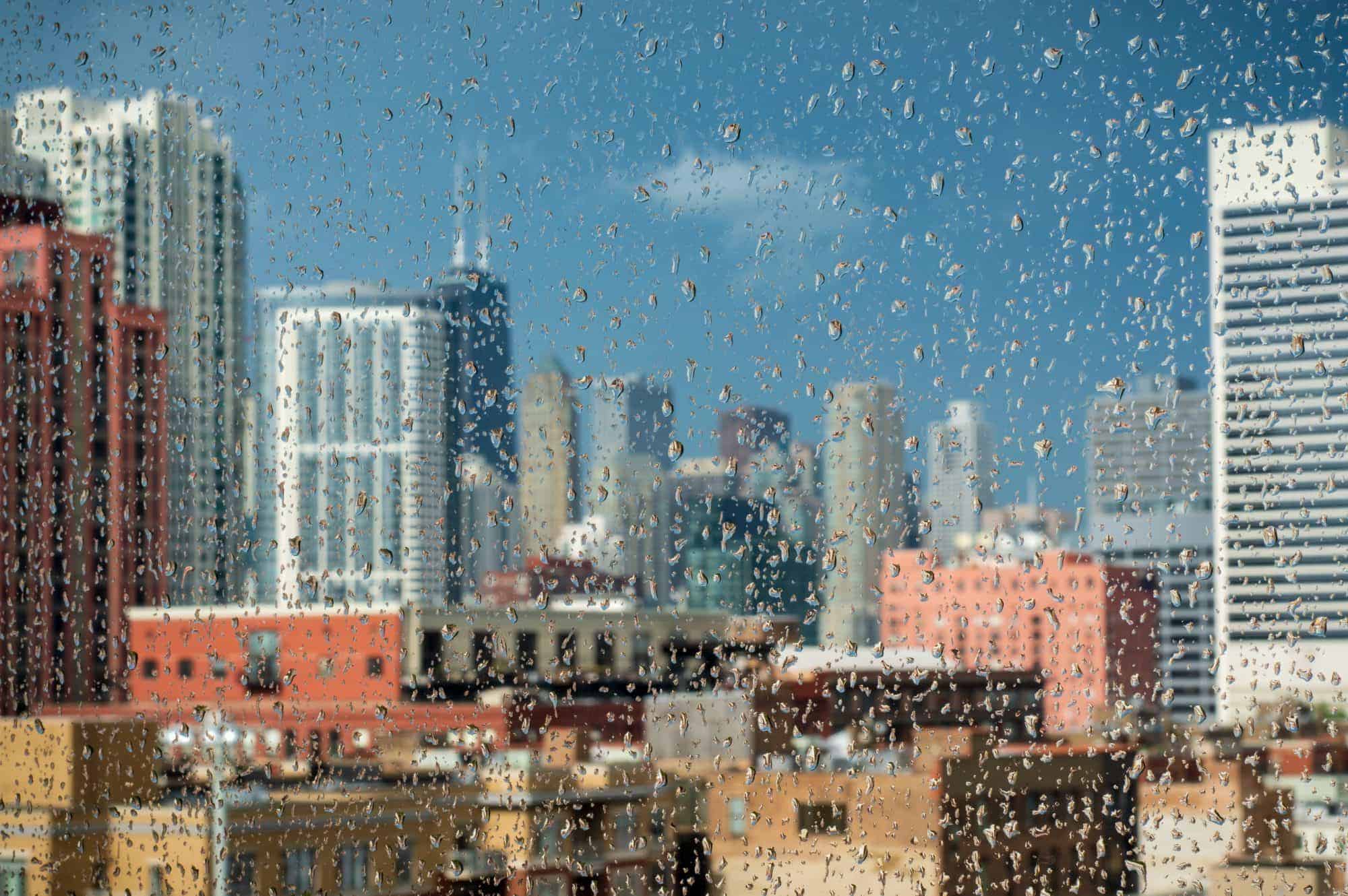 Raindrops on a window with a blurred view of Chicago buildings and skyscrapers, for outings with coworkers look into Chicago Brewery Tours.