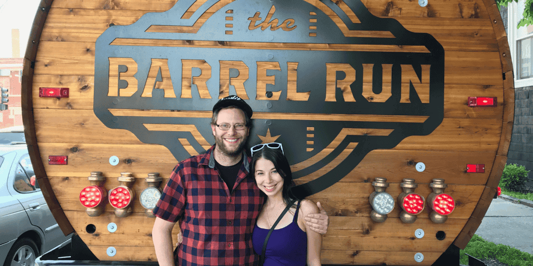 two people posing in front of The Barrel Run logo on the barrel bus in chicago