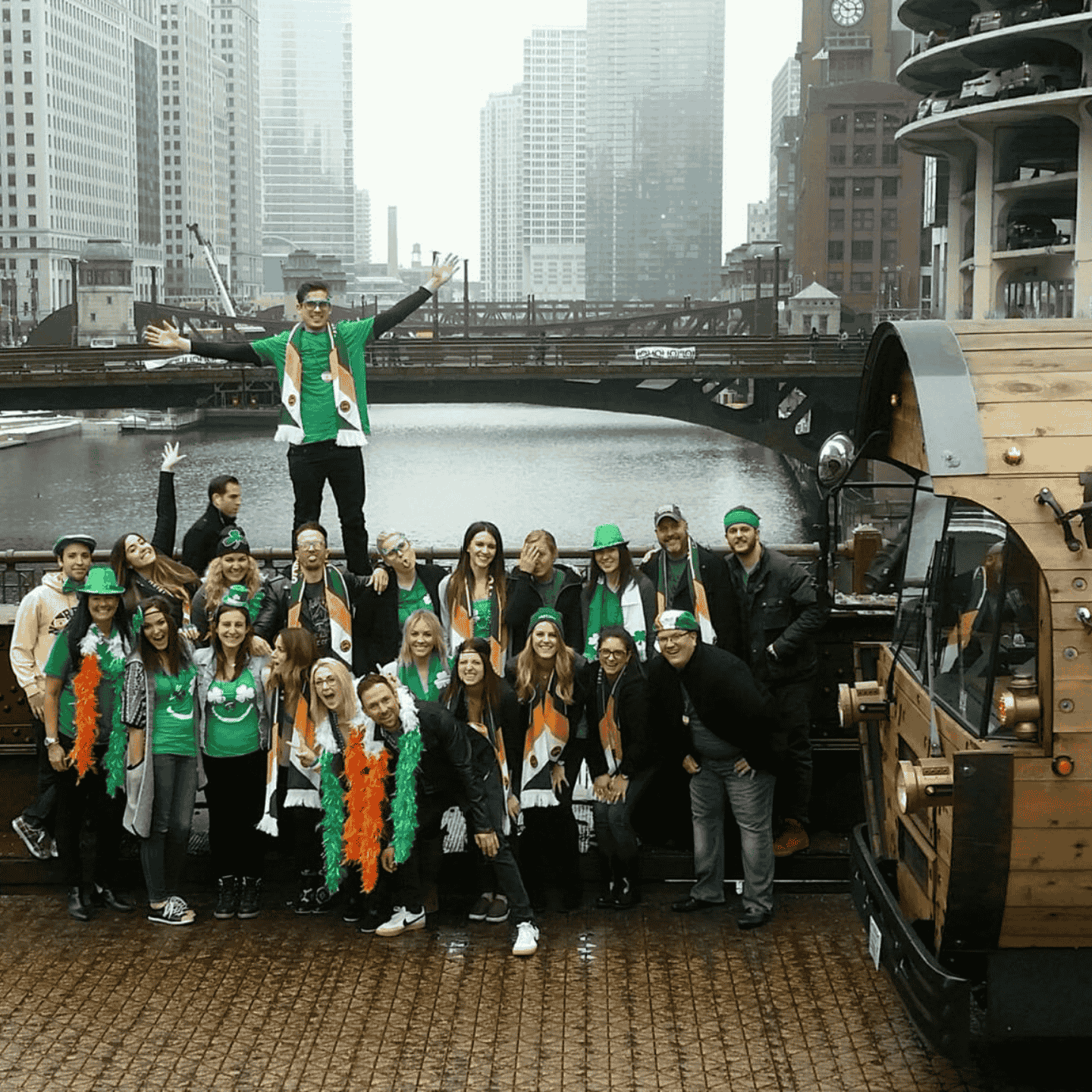 people dressed in orange and green celebrating St. Patrick's Day next to the barrel bus with skyscrapers in the background